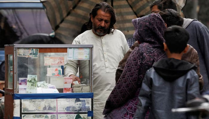 A currency broker stands near his booth, which is decorated with pictures of currency notes, while dealing with customers, along a road in Karachi on January 27, 2023. — Reuters