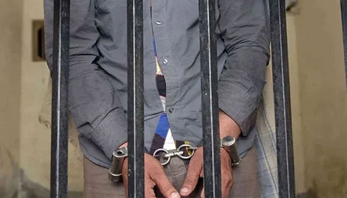 A representational image showing a person handcuffed and standing behind bars. — AFP/File